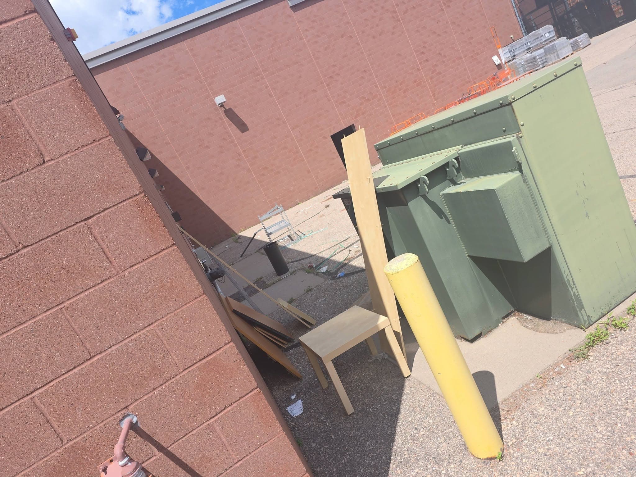 Wood panels and a small table set beside a commercial dumpster in a loading area for removal.