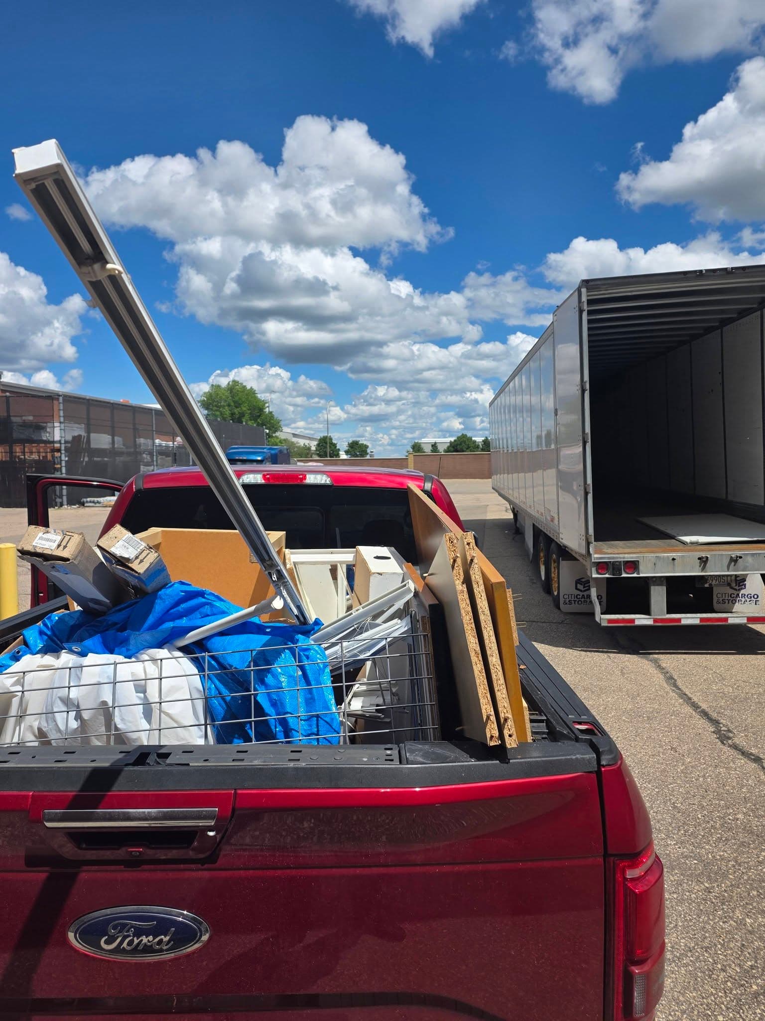 Red pickup loaded with mixed material beside a commercial loading area and box truck.
