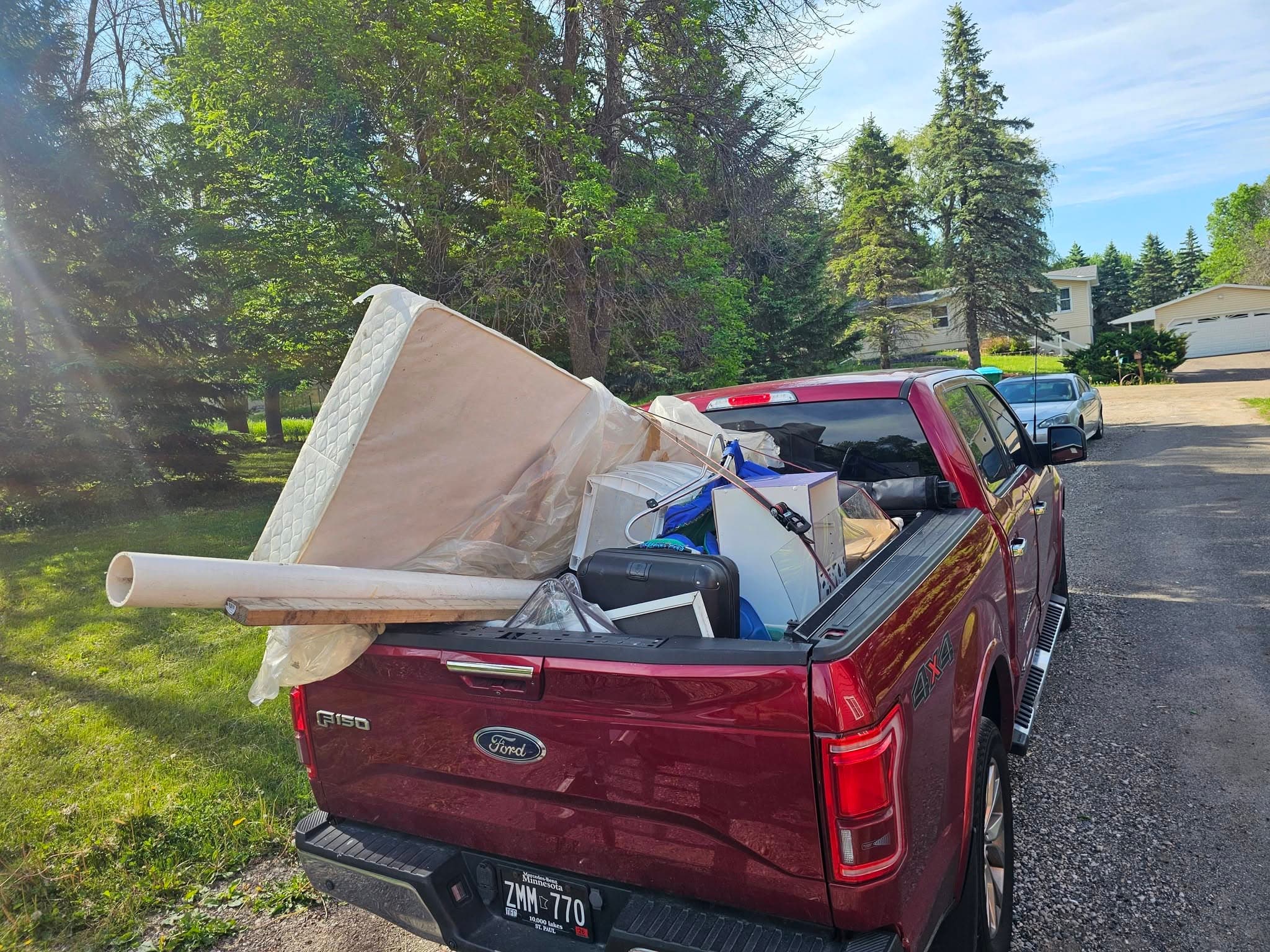 Red pickup loaded with a mattress, boxes, rolled material, and mixed household items in a residential driveway.