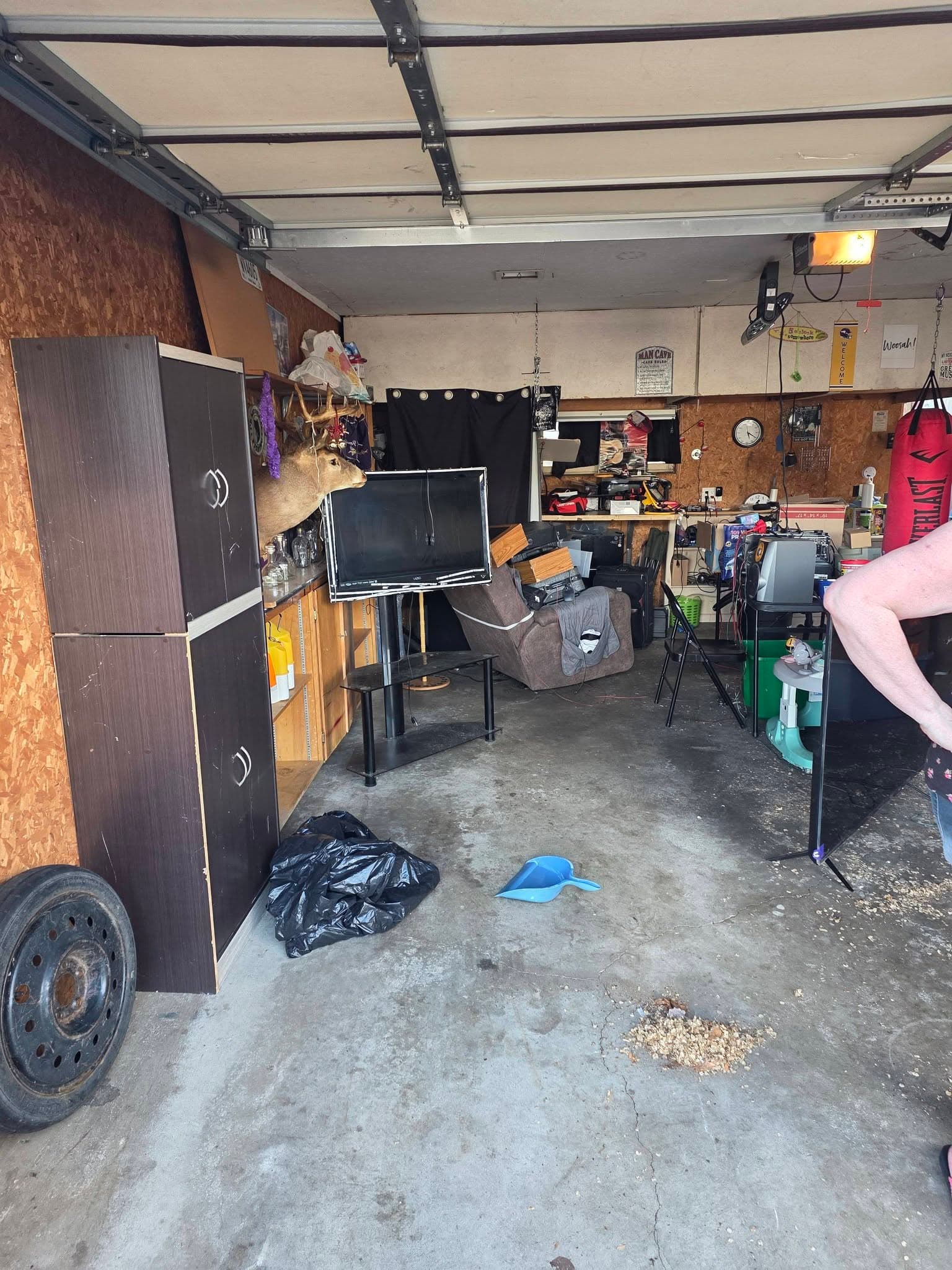 Garage containing cabinets, a television, an upholstered chair, bags, and assorted household items before removal.