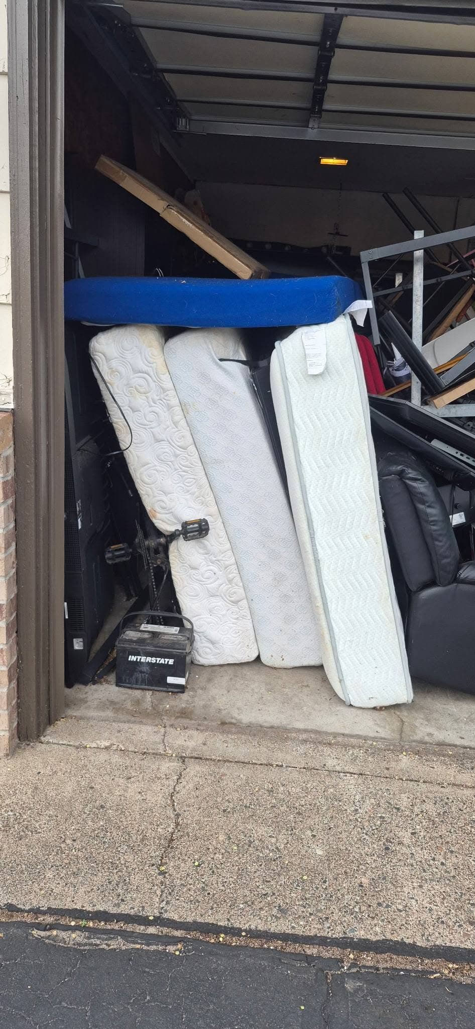 Three mattresses and assorted bulky household items staged inside an open garage for removal.