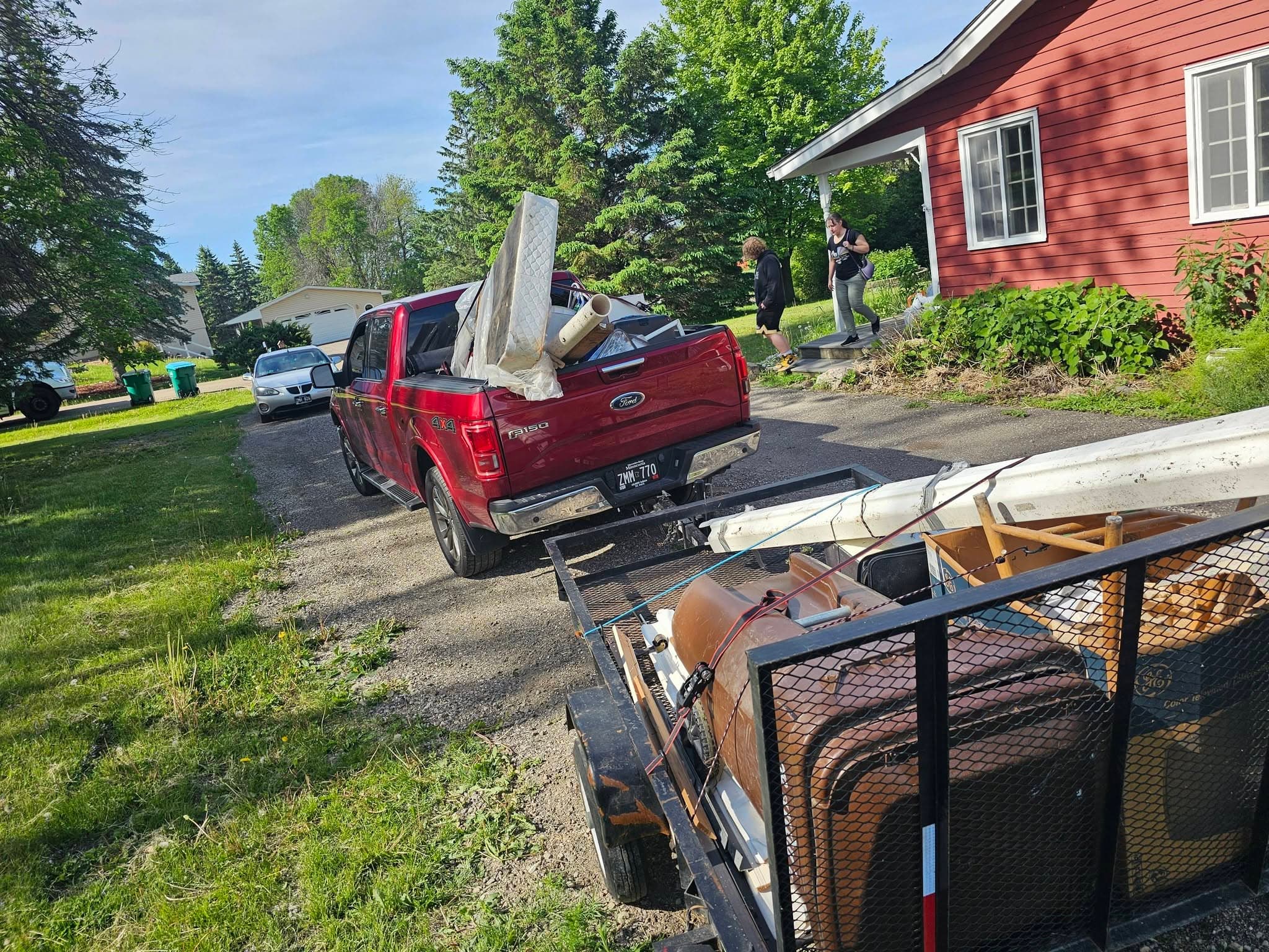 Royal Family red pickup and utility trailer loaded with household items in a residential driveway.