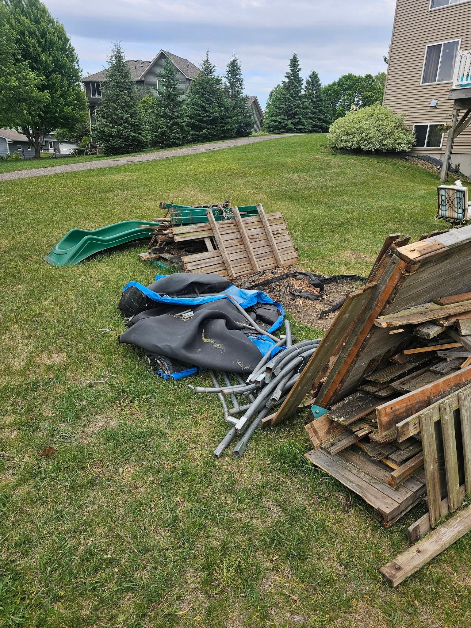 Dismantled playset lumber, a green slide, outdoor matting, and metal pieces gathered into pickup piles on a lawn.