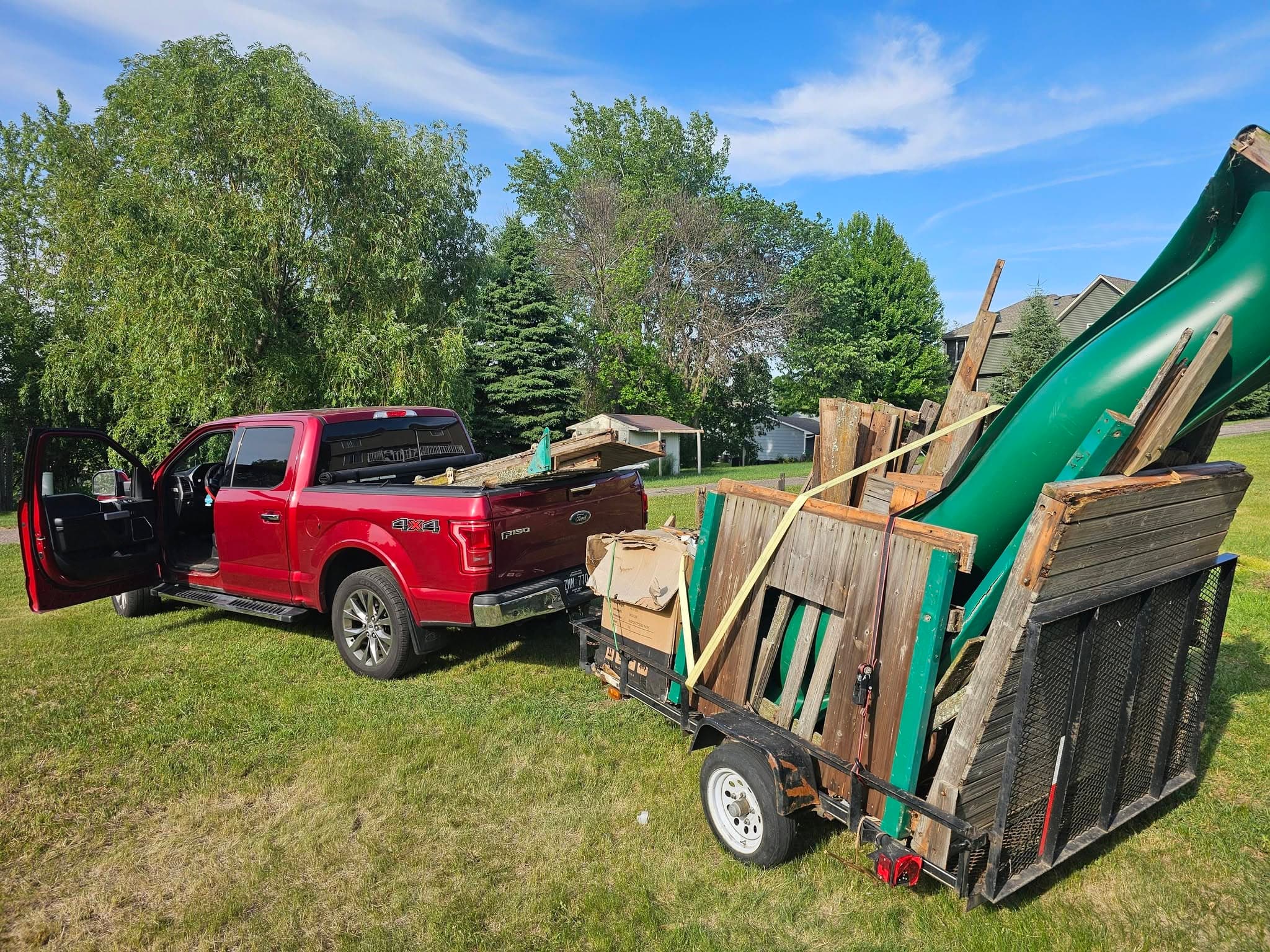 Red pickup and utility trailer loaded with dismantled wood and outdoor playset material.